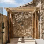 Custom backyard design with wood shade structure, outdoor shower and black beach pebble stones.