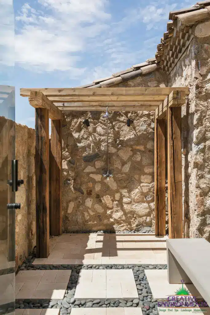 Custom backyard design with wood shade structure, outdoor shower and black beach pebble stones.