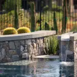 Custom backyard design with zero-edge pool, water feature into pool and curved retention wall.