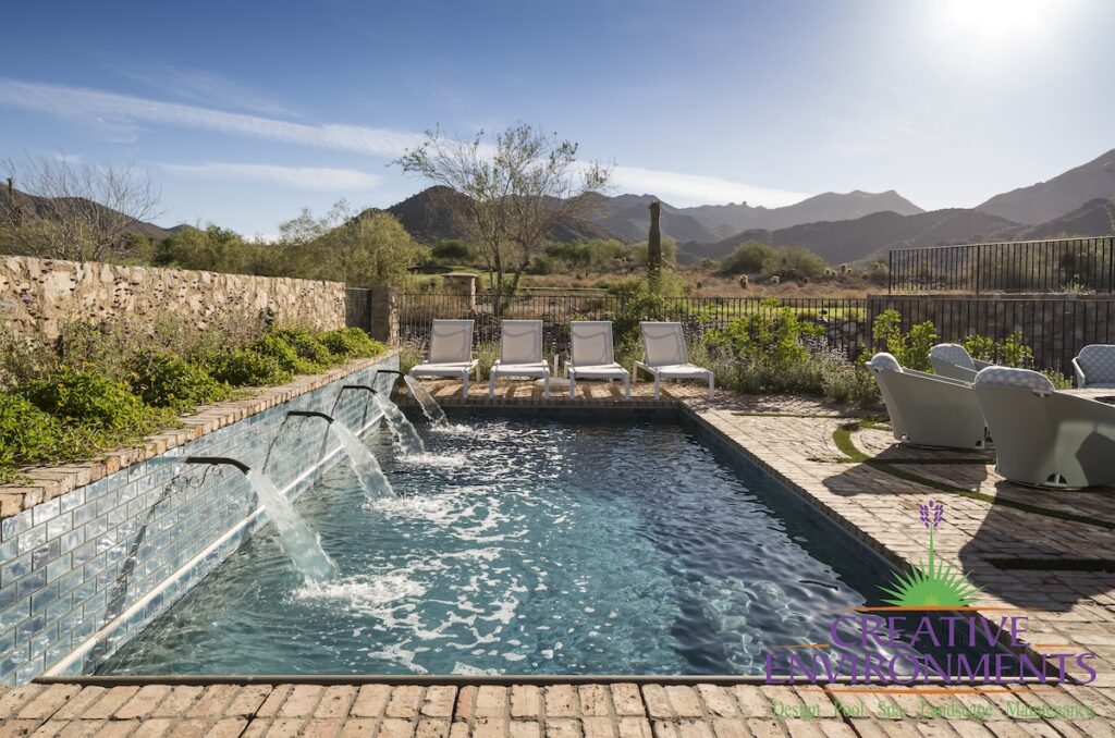 Custom backyard design with water scuppers into pool, multiple seating areas and brick deck.