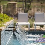 Custom metal water scuppers into pool with flowers.