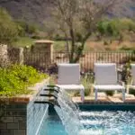 Custom water scupper feature into pool with metal fencing and chaise lounges.