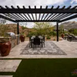 Custom backyard design with slatted metal shade structure, artificial turf and multiple seating areas.