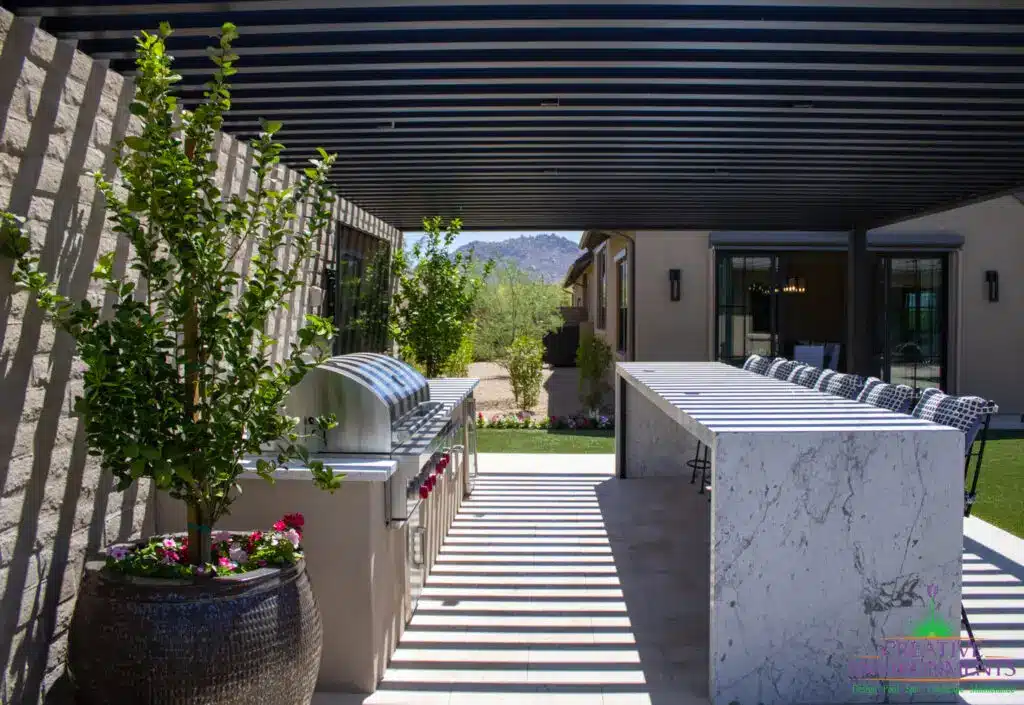 Custom backyard design with slatted metal shade structure, outdoor BBQ and bar seating.