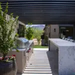 Custom backyard design with slatted metal shade structure, outdoor BBQ and bar seating.