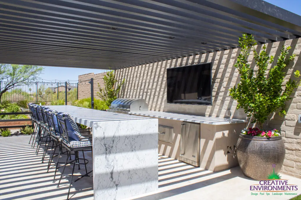 Custom backyard design with slatted metal shade structure, bar seating and large planters.