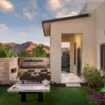Custom backyard design with traditional fireplace, artificial turf and uplighting on trees.