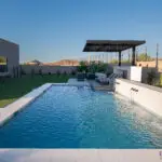 Custom backyard design with metal scupper water feature into blue pool, cantilevered shade structure and artificial turf.