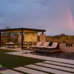 Custom backyard design with artificial turf, metal shade structure and natural stone accents.