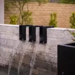 Custom backyard design with metal scupper water feature, pool retention wall and desert plants.