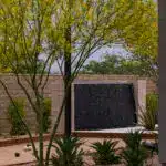 Custom backyard design with textured water wall, bocce ball court and organized planting.