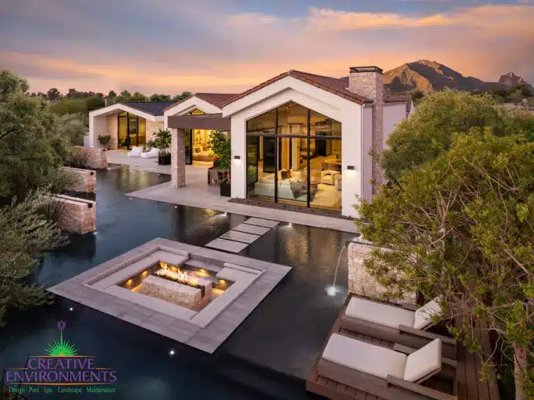 Custom backyard design with sunken fire pit inside unique-shaped pool, water features into pools and Jesus steps.