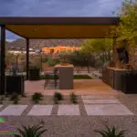 Custom backyard design with paver steps, metal shade structure and outdoor bar seating.