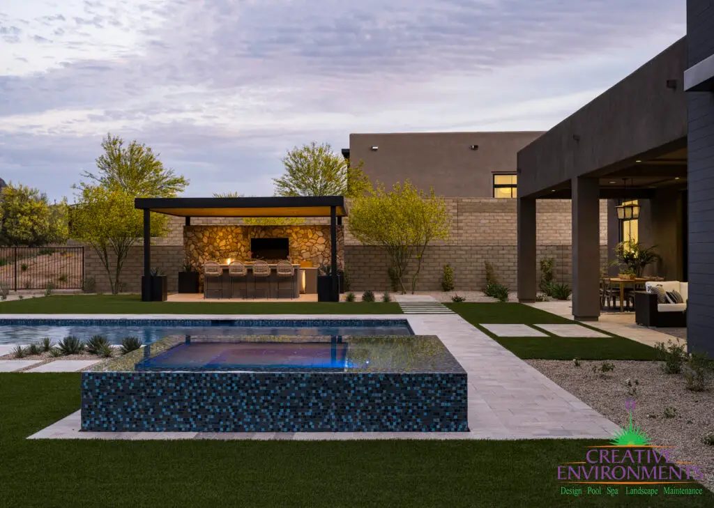 Custom backyard design with blue raised spa, artificial turf and metal shade structure.