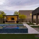Custom backyard design with blue raised spa, artificial turf and metal shade structure.