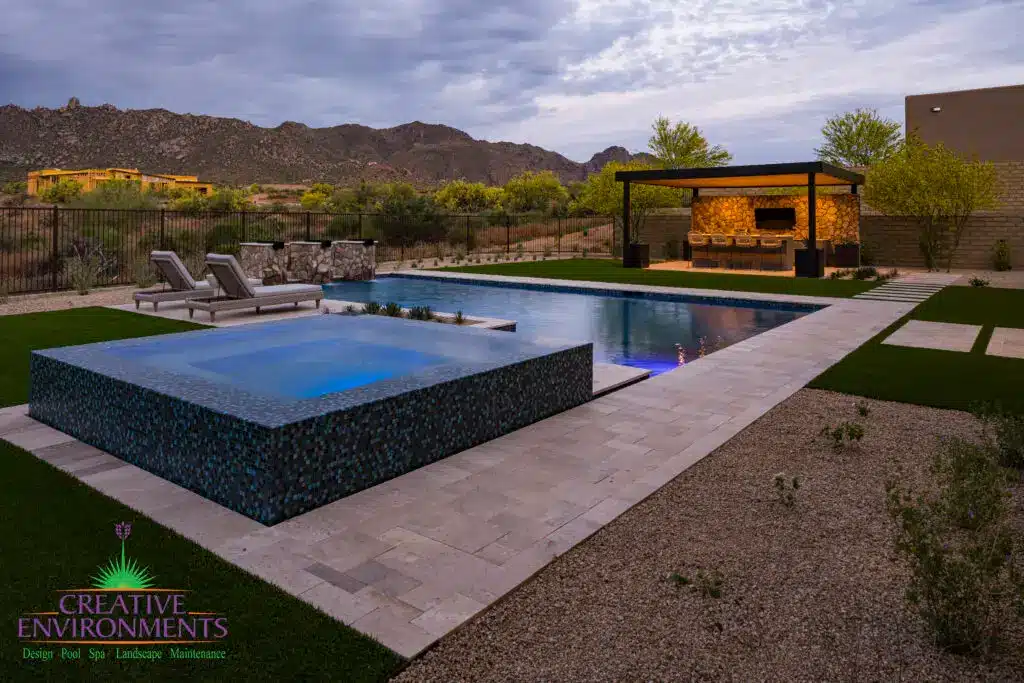Custom backyard design with natural stone decking, blue raised spa and metal shade structure.