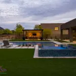 Custom backyard design with raised blue spa, artificial turf and metal shade structure.