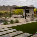 Custom backyard design with slatted metal shade structure, natural stone steps and artificial turf.