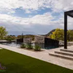 Custom backyard design with multiple water features, raised outdoor entertainment area and artificial turf.