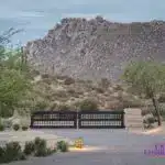 Custom front metal entry gate with desert plants, brick roundabout driveway and up lighting.