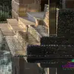 Custom black pebble stone water feature into pool.