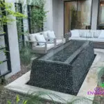 Custom backyard design with metal trellis and black pebble water feature.