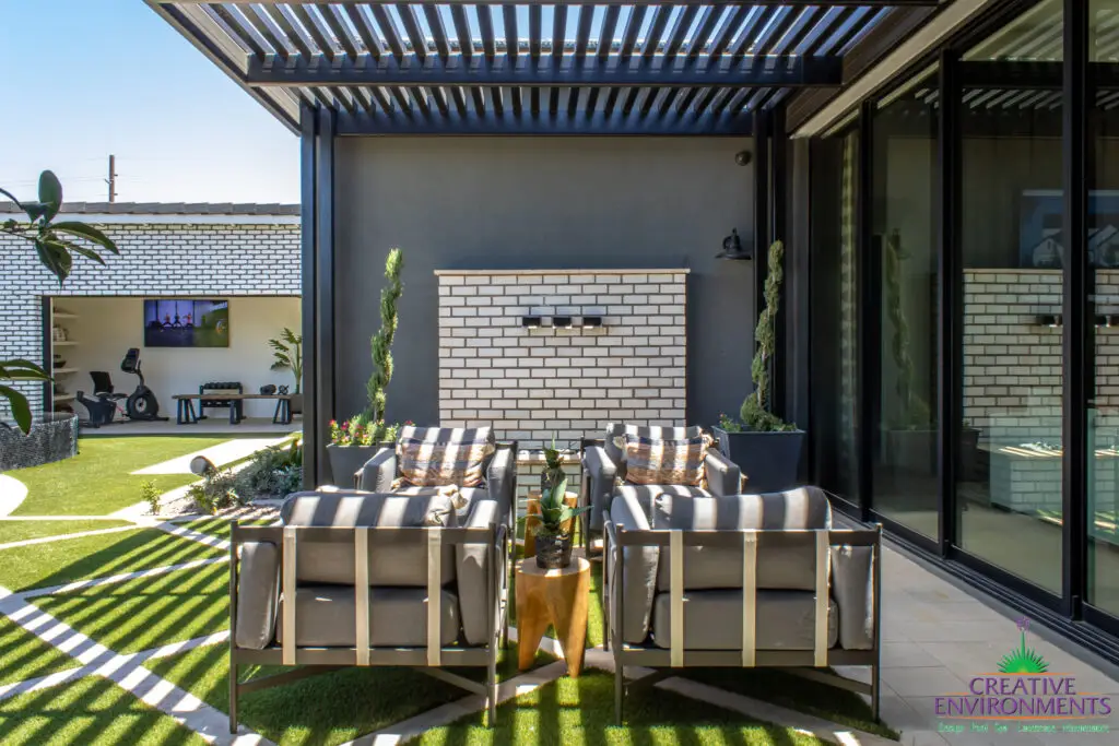 Custom backyard design with slatted metal shade structure, topiaries and artificial turf pattern.