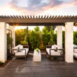 Custom backyard design with slatted shade structure, hanging daybed and privacy hedges.