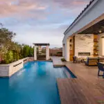 Custom backyard design with metal trellis, slatted shade structure and blue pool.