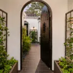 Custom front entryway with metal trellis, arched doorway and greenery.