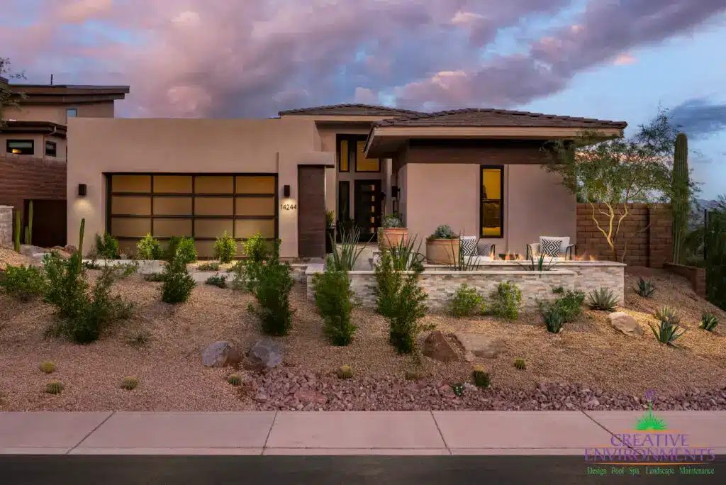 Custom front yard design with privacy wall, organized planting and fire table with outdoor seating.