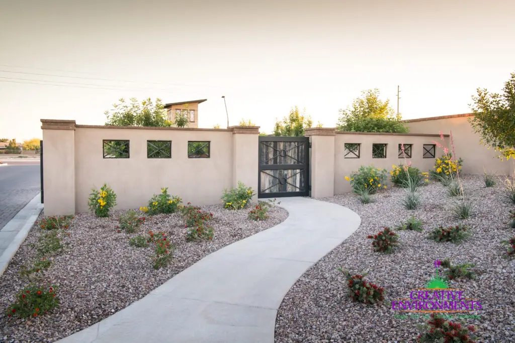 Custom community entrance with metal door, concrete pathway and organized planting.