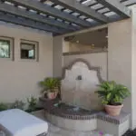 Custom backyard design with slatted shade structure, water feature and planters.