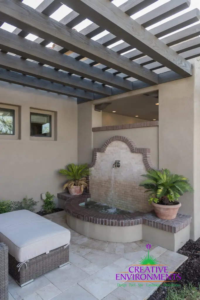 Custom backyard design with slatted shade structure, water feature and planters.