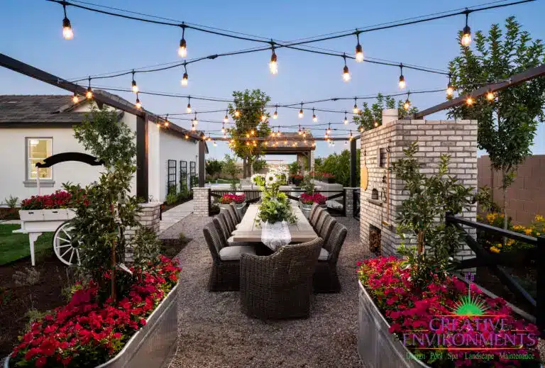 Custom backyard design with string lights, outdoor dining area and multiple planters filled with annuals and small trees.