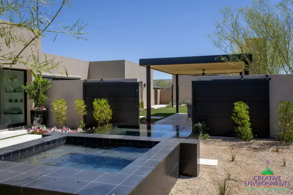 Custom backyard design with metal shade structure, raised spa and metal privacy gate.