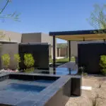 Custom backyard design with metal shade structure, raised spa and metal privacy gate.