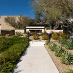 Custom entryway with organized planting, metal fencing and tree.