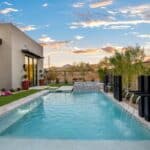 Custom backyard design with metal scupper water feature into blue pool and deco-tile, raised spa.
