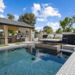 Custom backyard design with large potted plants, deco-tile pool and black water wall.