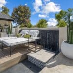 Custom backyard design with black water wall, large potted plants and multiple seating areas.