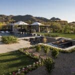 Custom backyard design with sunken entertainment area with cantilevered fire table, large, black pool and artificial grass.