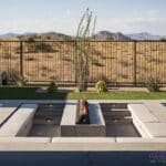 Custom backyard design with sunken fire pit, artificial turf and metal fencing.