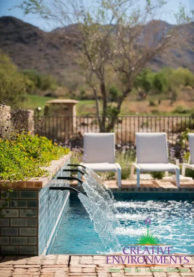 Custom water scupper feature into pool with metal fencing and chaise lounges.