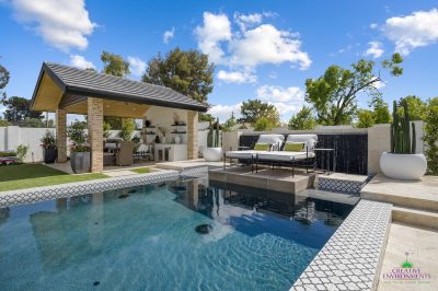 Custom backyard design with large potted plants, deco-tile pool and black water wall.
