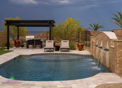 Custom backyard design with unique-shaped pool, metal scupper water feature into deco-tile pool and multiple seating areas.