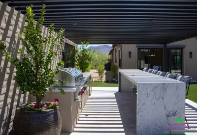 Custom backyard design with slatted metal shade structure, outdoor BBQ and bar seating.