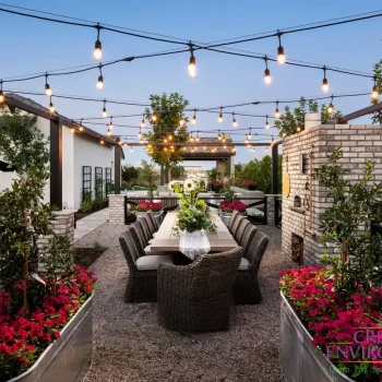 Weston (1) Custom backyard design with string lights, outdoor dining area and multiple planters filled with annuals and small trees.