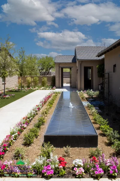 Custom front yard design with black water feature, organized planting and privacy wall.
